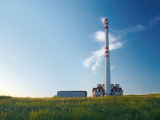 Waste incinerator in the evening sunlight, standing on a green meadow under blue sky. - obrazy, fototapety, plakaty