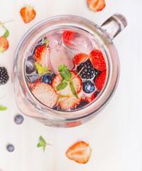 Jug with berries Infused Water and  ice cubes on  white wooden background, top view. Healthy summer...