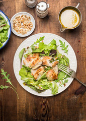 Chicken salad with green salad leaves, pine nuts and olive oil dressing. Healthy diet salad on rustic wooden background, top view. Country chicken salad.