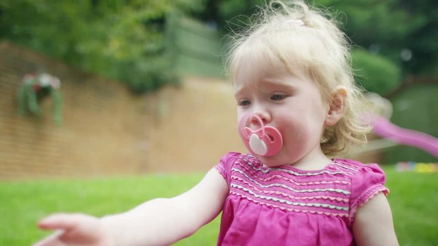  Portrait of little girl with pacifier & soft toy sitting in the garden
