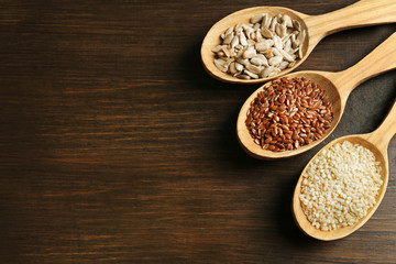 Sesame, flax and sunflower seeds in wooden spoons on table, closeup