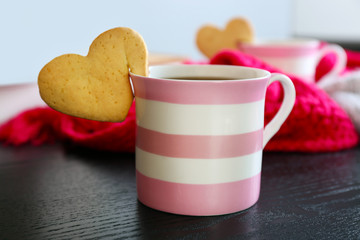 Heart shape cookie on cup of coffee on wooden table closeup
