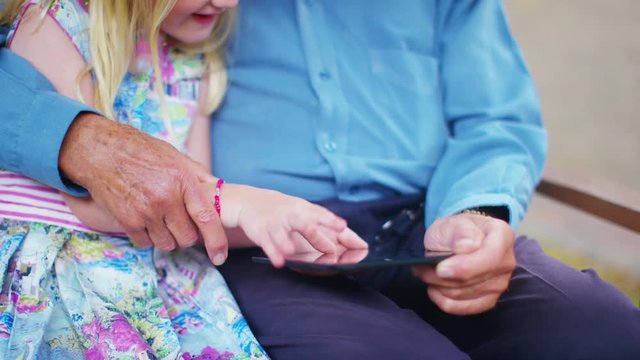  Grandfather & granddaughter sitting in the garden, looking at tablet computer