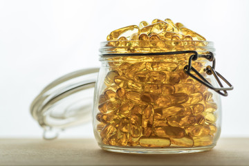 Omega 3-6-9 fish oil yellow softgels on wooden board into airtight glass jar