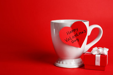 Cup with greeting card and gift box for Valentines Day on red background