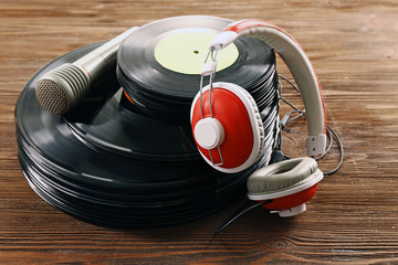 Stack of old vinyl records with headphones and microphone on wooden background
