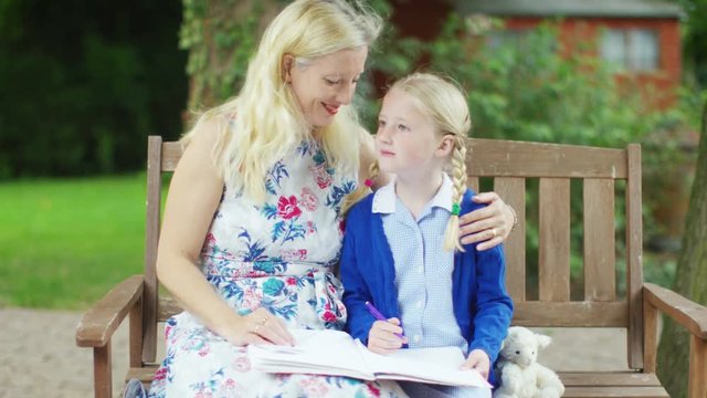  Affectionate mother and daughter sitting in garden together doing homework