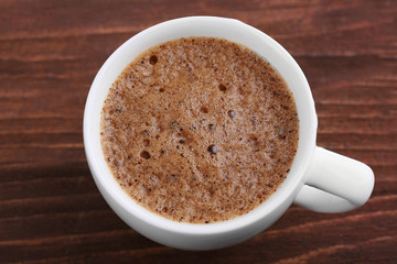 Cup of coffee with brown foam on wooden background, top view