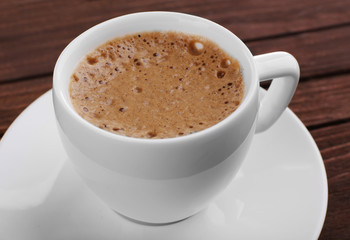 Cup of coffee with brown foam on wooden background, close up