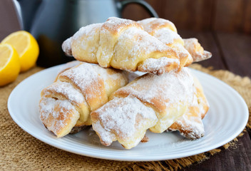 Sweet homemade lemon croissants with powdered sugar. Teapot