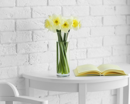 Fresh narcissus flowers and open book on wooden table on brick wall background
