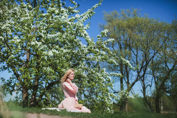 Naklejka na ściany i meble beautiful girl in dress sitting under the apple blossom