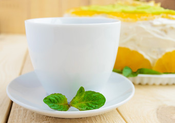 White cup of tea with a mint leaf close up on a light wooden background and fruit cake