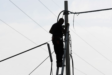 Elettricista lavoro all'aperto, su scala e palo elettrico, con cielo azzurro