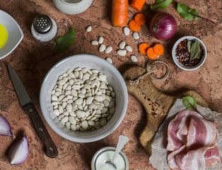 White beans, bacon, carrots, red onion, spices and herbs - ingredients for making bean mash with bacon. On a stone background. Top view