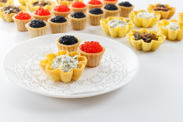 Tartlets filled with cheese and dill salad and caviar and plate with tartlets against white background