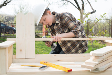 Teen boy in helmet with a screwdriver making a garden bench outdoor