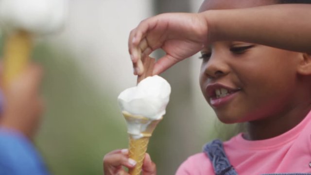  Portrait of  cute little girl enjoying an ice cream in the park with her brother. 