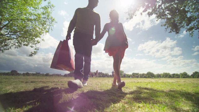  Happy mixed ethnicity couple expecting a baby, walking in park with shopping 
