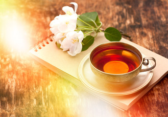 Tea cup, notebook and white spring flowers on a wooden table