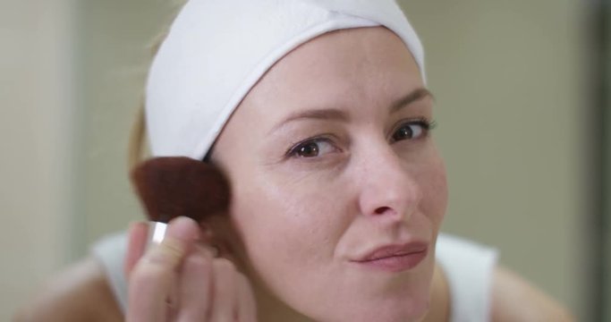  Close up portrait woman in bathroom looking in mirror & putting on makeup