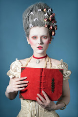 Baroque Style - amazed young woman with vintage red book posing over blue background in elegant light corset with lace. Renaissance. Rococo. Fashion.