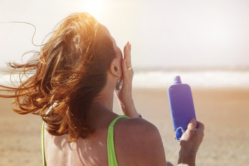 femme senior s'enduisant de crème solaire à la plage 