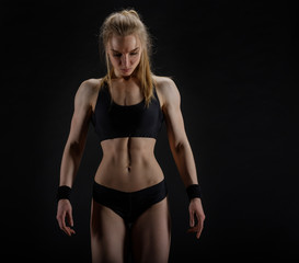 Young muscular woman posing on black