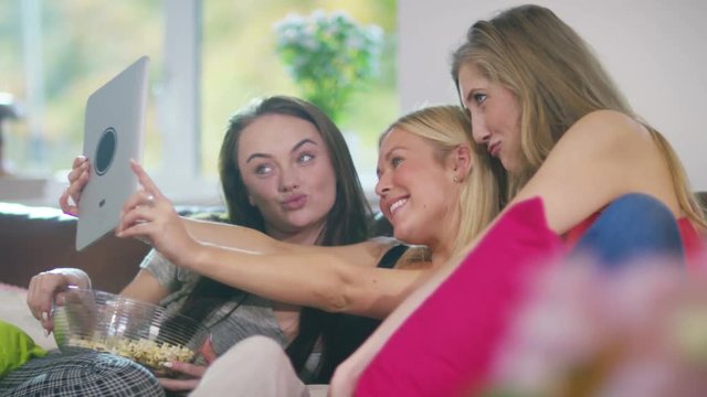  Young female friends at home pose for a selfie with computer tablet.