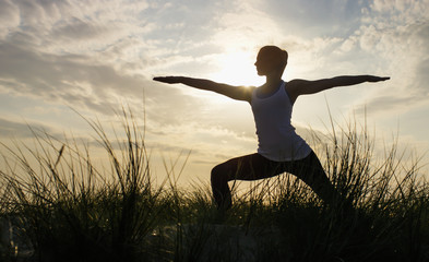 Silhouette of a young woman in a yoga warrior pose on a beach hilltop - 110620129