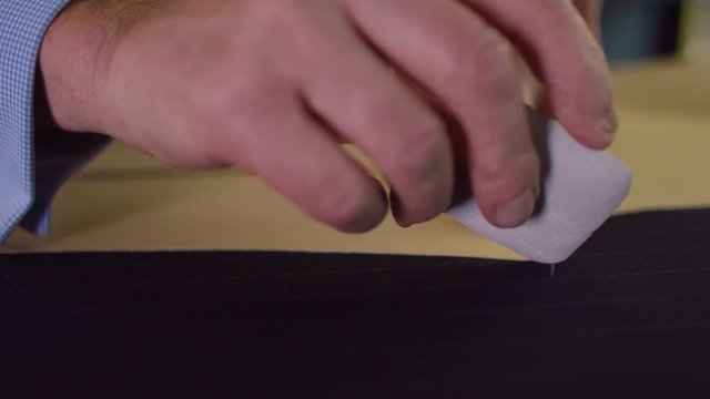  Close up on hands of a tailor working in his shop, drawing template on a piece of fabric. Shot on RED Epic.