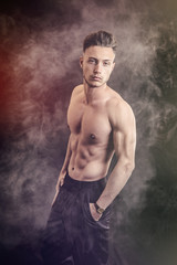 Fototapeta na wymiar Lean athletic shirtless young man standing on dark background