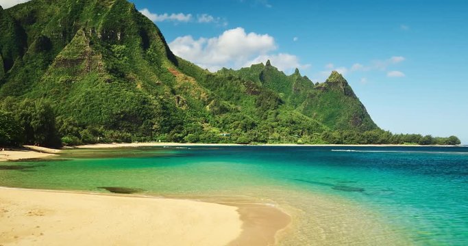 Aerial view flying over amazing white sand beach and tropical coral reef lagoon towards beautiful green mountains on Kauai
