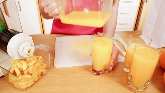 Woman make orange juice in juicer machine pouring drink in glass 4K