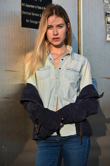 Fashion urban portrait of young, slim, beautiful model in denim shirt and jeans posing against metallic background.