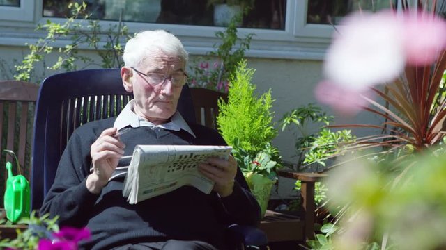  Elderly Man In The Garden Doing A Crossword Puzzle In The Newspaper