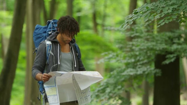  Man hiking in the woods on his own, looking at map and trying to find his way. 