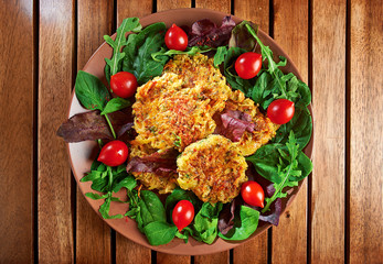 Homemade veg burgers from potatoes and lentils, served on a plate with tomatoes and green salad on a wooden background;  top view.