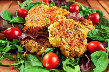 Homemade veg burgers from potatoes and lentils, served on a plate with tomatoes and green salad on a wooden background; close up.