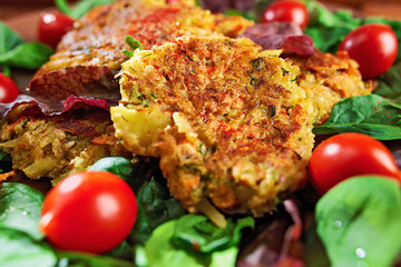 Homemade veg burgers from potatoes and lentils, served on a plate with tomatoes and green salad on a wooden background; close up.