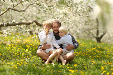 Naklejka na ściany i meble Portrait of Happy Father and Two Young Children Hugging on a Spring Day in a flowering Apple Orchard