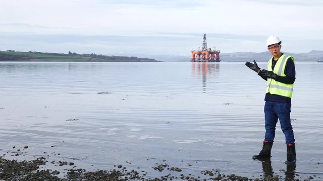 An asian engineer standing in front of semi submersible oil rig in Invergordon Scotland
