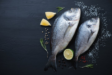 Sea breams with seasonings on a black wooden surface, above view