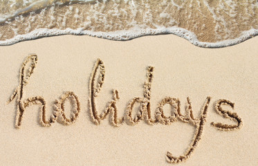 Word Holidays handwritten on sand