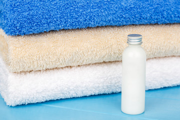 Three towels with one little bottle of shampoo on a blue wooden