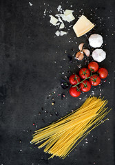 Food frame. Pasta ingredients. Cherry-tomatoes, spaghetti pasta, garlic, basil, parmesan and spices on dark grunge backdrop, copy space
