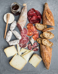 Cheese and meat appetizer selection or wine snack set. Variety of italian cheese, salami, bresaola, baguette, honey on over grey concrete backdrop, top view.