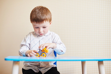 Little boy playing with colored toy car on a table