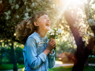Happy teenage girl in the sunlight. Emotions - happiness, joy. Woman laughing happily. Park dawn. Flowers of apple, apple orchard. 