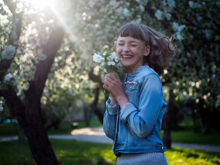 Happy teenage girl in the sunlight. Emotions - happiness, joy. Woman laughing happily. Park dawn. Flowers of apple, apple orchard. 